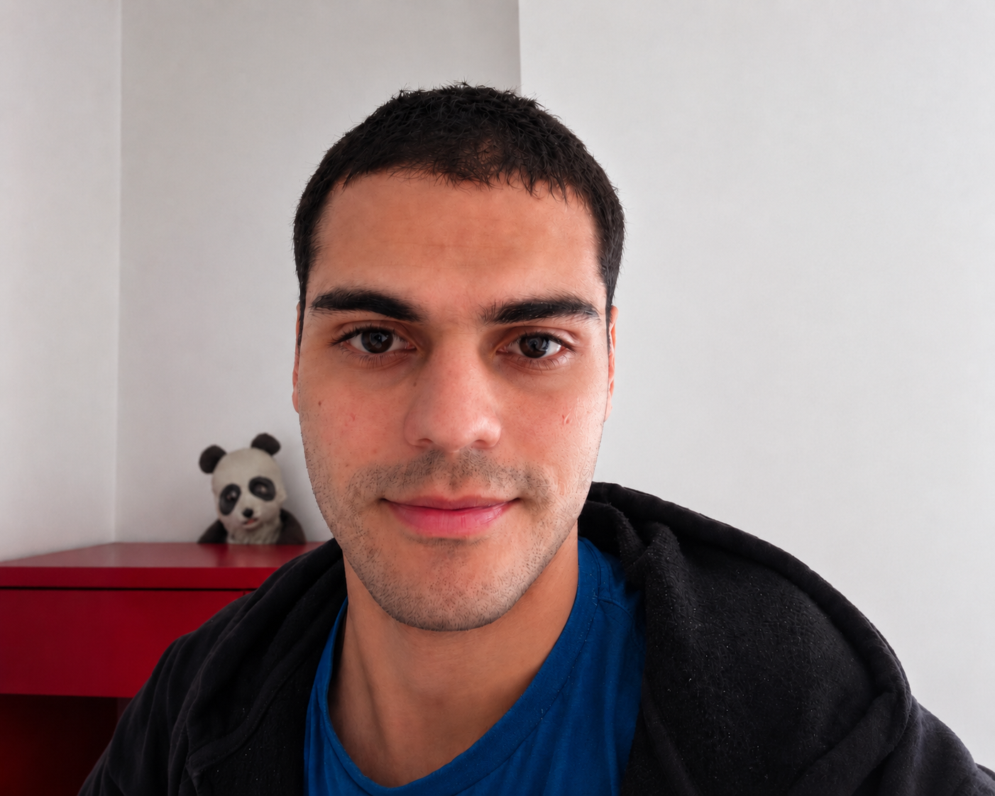 Petros sorrindo, com um panda de pelúcia ao fundo